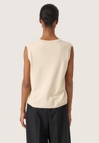Pull crème sans manches avec un col rond, texture douce et coupe décontractée, associé à un pantalon noir à jambes larges.