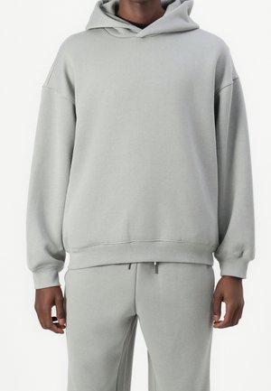 Ljusgrå huvtröja i mjuk bomullsblandning med lös passform, sänkta axlar och en kenguruficka. Mjuk textur med ribbade muddar.