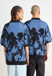 Πλεκτό πουλόβερ κοντό μανίκι σε μπλε χρώμα με μαύρο αφηρημένο μοτίβο, διαθέτει στρογγυλή λαιμόκοψη και μαύρη ribbed λεπτομέρεια στα μανίκια και το στρίφωμα.