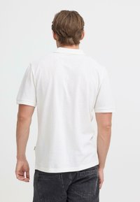 Polo blanc en coton texturé, doté d'un col classique et de manches courtes. Le corps est légèrement ample avec un ourlet droit.
