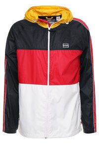 Kurtka przeciwwiatrowa Levi's z blokami kolorów: czarny na górze, czerwony w środku, biały na dole, żółty kaptur i zapięcie na suwak z przodu.