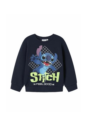 Tumedatehnikasviit, millel on Stitchi graafika, erksate roheliste tähtedega "STITCH FEEL GOOD" ja ruudustik taustal tegelase taga.
