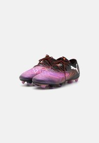 Bottines de football noires et violettes avec surface texturée, lacets orange, et crampons pour terrain ferme. Présente un logo de marque blanc sur le côté.