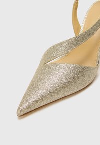 Kuldne sädelev slingback konts, millel on terav nina, ristuvad rihmad ja sile sisepinna vooder. Tundub libisemisvastane talla detail.