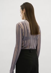 Langsleeve top van lichtgewicht, gestructureerde stof met verticale strepen in gedempt paars en beige; gecombineerd met zwarte broek.