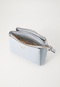 Sac bandoulière bleu clair en matériau texturé avec deux compartiments zippés, quincaillerie dorée et un accent logo à l'avant.