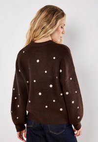 Maglione marrone a maglia con dettagli floreali bianchi, silhouette oversize, scollatura rotonda e maniche lunghe con polsini a coste.