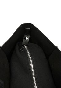 Interiér čiernej tašky s uzáverom na zips, textúrovanou tkaninou a koženým popruhom s kovovým prvkom. Jednoduchý, priestranný dizajn.