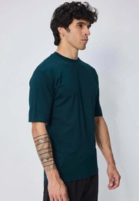 T-shirt à manches courtes en bleu canard foncé avec un col rond. Fabriqué en tissu lisse et léger. Présente une coupe décontractée et un design minimaliste.