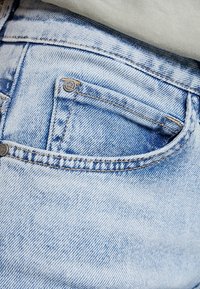Jeans in denim azzurro chiaro con tasca posteriore caratterizzata da dettagli di cucitura e un leggero effetto acid-wash, che mette in evidenza un aspetto texturizzato.