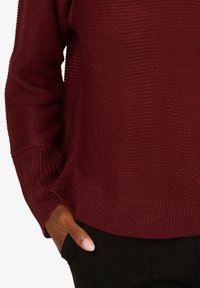 Burgunderfarbener Strickpullover mit strukturiertem Muster, Rippbündchen und -saum, ausgestattet mit seitlichen Taschen und einem lässigen Schnitt.