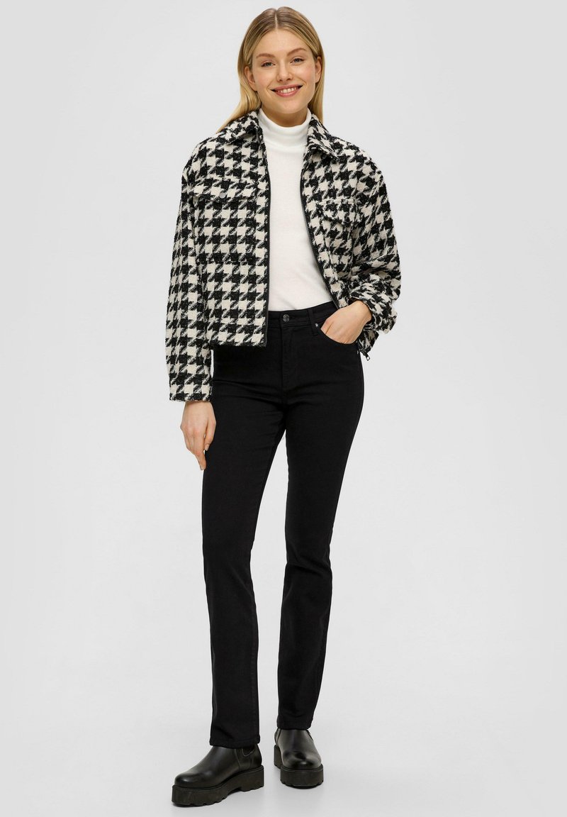 Schwarz-weiße Hahnentrittjacke mit kurzem Schnitt, kombiniert mit schwarzen engen Jeans und schwarzen Plateaustiefeletten.