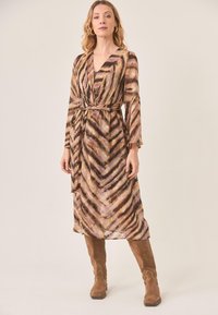 Vestido largo tipo envoltura en tela transparente con un patrón de zigzag en marrón y púrpura, con mangas largas y un cinturón a juego.