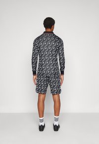 Sportswear sæt bestående af en langærmet top og shorts, lavet af mønstret stof i sort og grå, med kontrasterende røde detaljer på kraven.