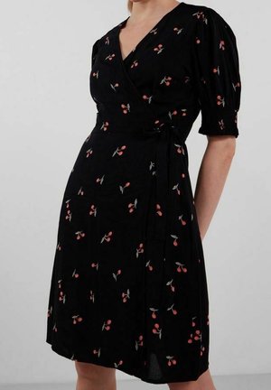 Robe portefeuille noire avec manches courtes bouffantes et imprimé cerises rouges, nouée à la taille, portée par un modèle partiellement visible.