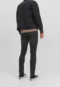 Svart denimjacka med rak passform, bärs över en ljus beige skjorta och svarta slim-fit jeans, tillsammans med svarta sneakers.