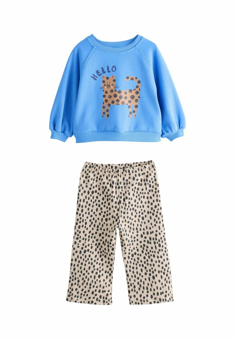 Blauwe sweatshirt met een grafische afbeelding van een bruin gevlekte kat en tekst die zegt "HELLO," gecombineerd met beige broek met zwarte stippenpatronen.