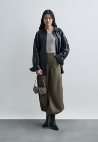 Camicia over-size in pelle nera, maglione grigio aderente, pantaloni larghi oliva, stivali neri al ginocchio e una piccola borsa grigia con hardware dorato.