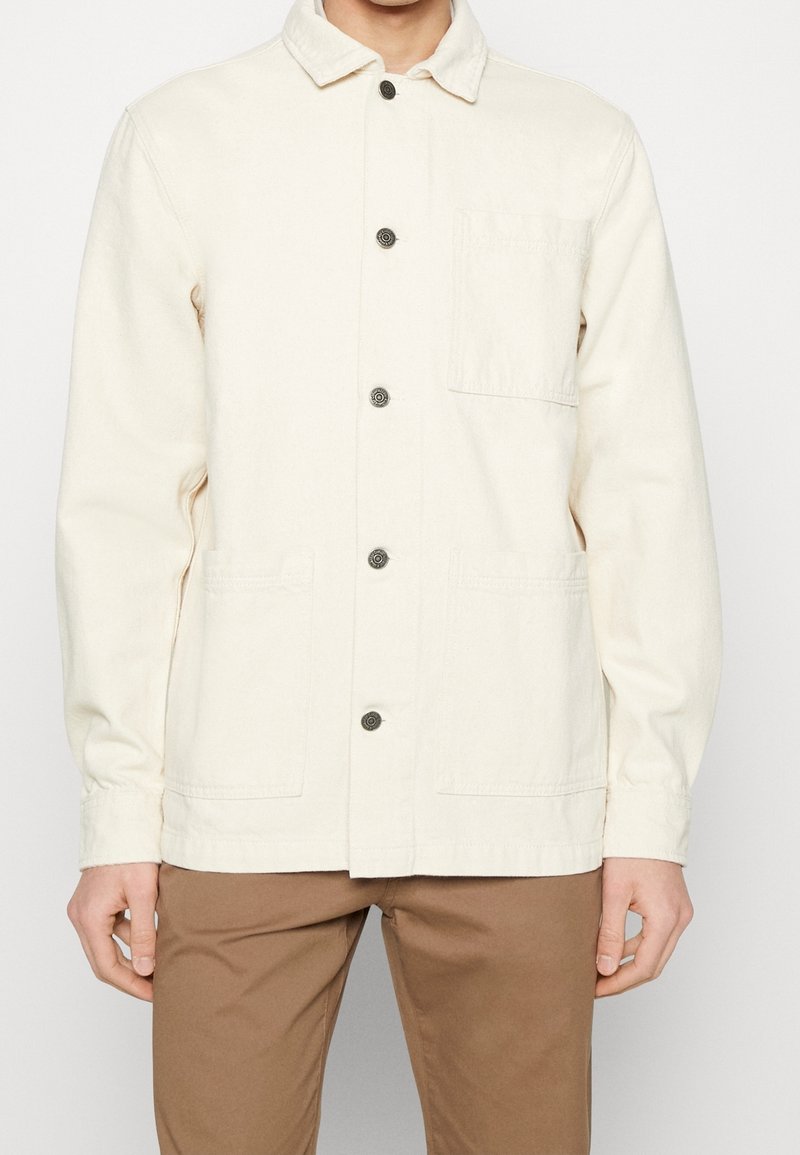Jasnobeżowa kurtka z płótna z kołnierzem, z przodu zapinana na guziki, z dwoma bocznymi kieszeniami i jedną kieszenią na piersi. Materiał o fakturze, luźny krój.
