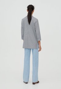 Checked oversized blazer in black and white, lightweight fabric, asymmetric hem, paired with high-waisted light blue jeans, flared fit.