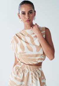 Viegla, īsa topiņa ar bēšā un baltā krāsā dzīvnieku rakstā, ar vaļēju piegriezumu un plašu kakla izgriezumu. Saskaņota ar augsta vidukļa svārkiem.