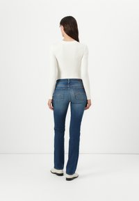 White long-sleeved top paired with blue denim jeans. Jeans feature classic 5-pocket styling and subtle stitching on the back pockets.