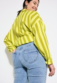 Zeleno-žlutě pruhovaná košile na knoflíky spárovaná se světle modrými džíny s kapsou ve tvaru srdce. Hladký materiál, uvolněný střih.