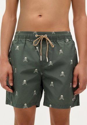 Shorts de baie verzi cu un model repetat de craniu și oase încrucișate, talie elastică cu șnur bej și buzunare laterale.