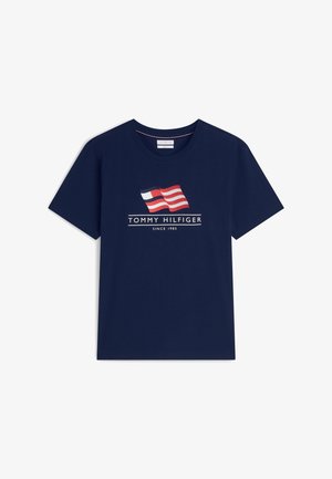 Κοντομάνικο μπλουζάκι σε ναυτικό μπλε με γραφικό κυματιστής σημαίας σε κόκκινο, άσπρο και μπλε πάνω από το κείμενο "Tommy Hilfiger Since 1985" στο μπροστινό μέρος.