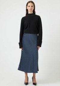 Czarny sweter z długimi rękawami, zestawiony z granatową spódnicą midi w groszki z jasnoniebieskimi kropkami. Modelka ma na sobie czarne szpilki.