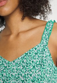 Top verde con estampado que presenta un escote en V profundo, tirantes texturizados con bordes con volantes y una tela suave y ligera.