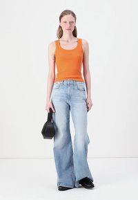 Oransje ribbet tanktop, lyseblå flagrende jeans og en svart geometrisk veske. Modellen står mot en enkel hvit bakgrunn.