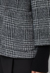 Czarny i szary wzorzysty sweter z dzianiny o puszystej fakturze, z kieszenią i prążkowanymi czarnymi mankietami.