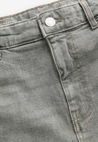 Szare dżinsy mają klasyczny pięciopocketowy design, uwydatniony kontrastującymi brązowymi szwami oraz srebrnym guzikiem. Miękka faktura i lekki materiał.