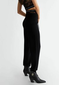 Czarne dzianinowe spodnie o luźnym kroju, z elastycznym paskiem na sznurku. Połączone z czarnymi botkami za kostkę z geometrycznym złotym akcentem.