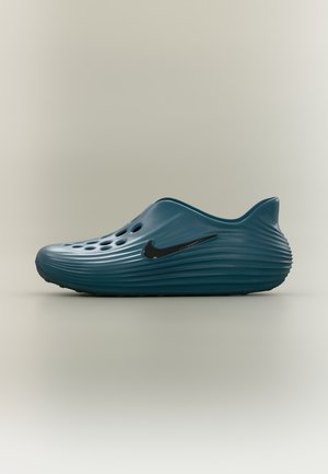 Тюркоазена обувка Nike без връзки с вентилационни отвори и набраздена подметка, показана в страничен профил на едноцветен фон.