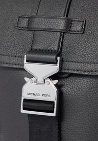Black leather bag with a textured finish. Features a silver metallic clasp with "MICHAEL KORS" engraved and a black strap.