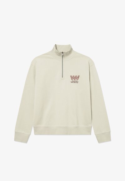 Ανοιχτό μπεζ μακρυμάνικο πουλόβερ με ραμμένη μανσέτα και τελείωμα, φερμουάρ τετάρτου και μικρό κόκκινο λογότυπο και κείμενο στο αριστερό στήθος.