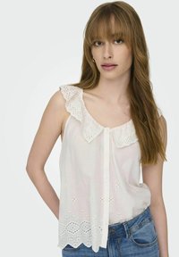 Blusa blanca con cuello con volantes, botones en la parte delantera y detalles de ojales en el dobladillo. Tejido ligero, corte relajado, combinada con jeans azules.