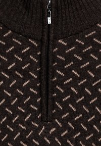 Donkerbruine rits-trui met een hoge ribbelkraag, voorzien van een geometrisch lichtbruine patroon en een centrale ritssluiting met gemarkeerde hardware.