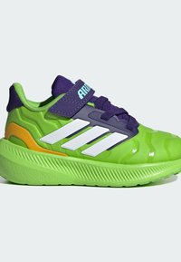 Green athletic shoe with a textured design, featuring purple accents, a Velcro strap, and three white stripes on the side. Rubber sole.