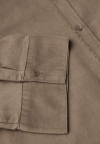 Détail d'une chemise en velours côtelé marron avec un col rabattu, un bouton et une texture côtelée visible. Accent sur le tissu et le design de couture.