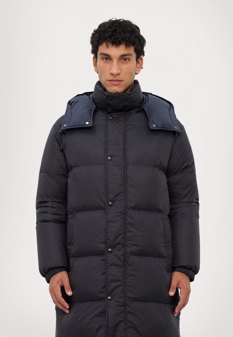 Zwarte pufferjas met een middellange stijl, drukknoopsluiting, hoge kraag en contrasterende blauwe afneembare capuchon. Glad, gewatteerd materiaal.
