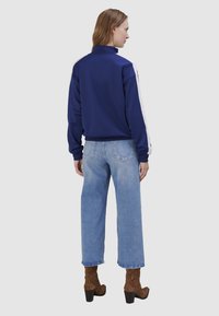 Pull bleu marine avec col montant et rayures blanches sur les côtés, assorti à un jean large bleu clair et des bottines à motifs marron.