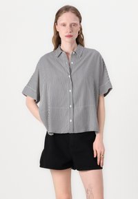 Camisa de botonadura corta de manga corta a rayas blancas y negras con cuello, que presenta un corte holgado y un diseño sin costuras en el dobladillo.