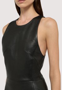 Svart ärmlös klänning i läder med rund halsringning, sidoutskärningar och subtila sömdetaljer för en strukturerad siluett.