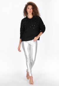 Fekete kötött pulóver vállain díszítéssel, fényes ezüst leggings-szel párosítva a letisztult megjelenésért. Tiszta és sima textúra.