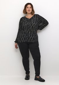 Czarna bluzka z teksturowanym wzorem białych linii, z dekoltem w serek, długimi rękawami, w połączeniu z czarnymi spodniami slim-fit i czarnymi loafersami.