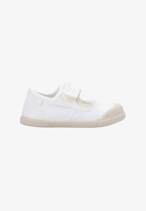 Zapatilla de lona blanca con dos correas de Velcro, suela de goma beige y punta redonda. Diseño minimalista con textura contrastante en la suela.