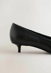 Svarta balettskor med låg klack, tillverkade av slätt syntetmaterial, med rundad tå och minimalistisk design.